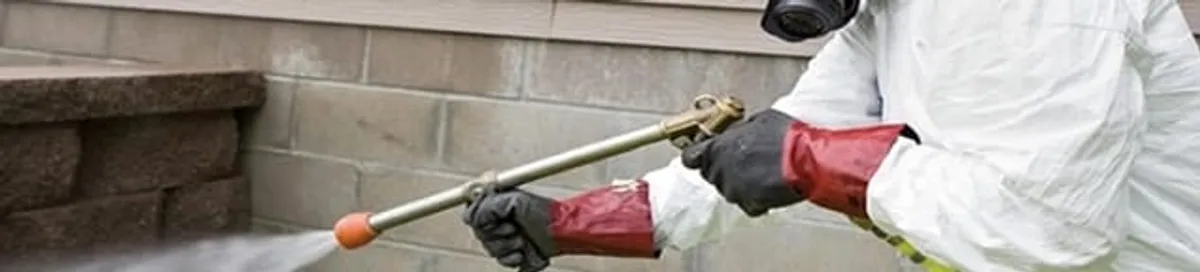 Pest control technician applying exterior insect treatment along a home foundation in Henderson, NV