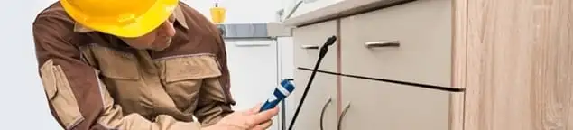 Roach exterminator applying treatment under kitchen cabinets in Henderson, NV
