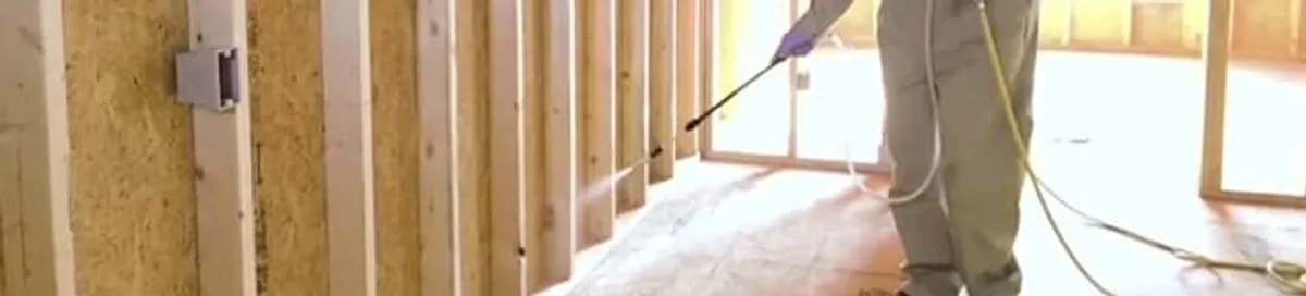 Termite treatment technician applying spray along framing and unfinished walls in Henderson, NV