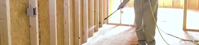 Termite treatment technician applying spray along framing and unfinished walls in Henderson, NV